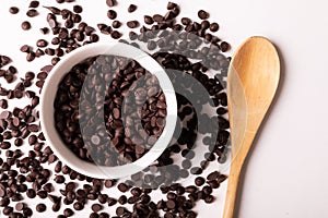 Overhead view of fresh chocolate chips with bowl and wooden spoon on white background