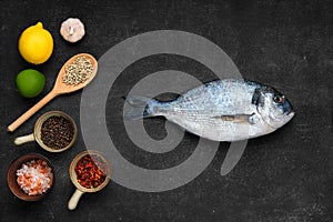 Overhead view of fresh raw gilt head bream with spice on black stone background