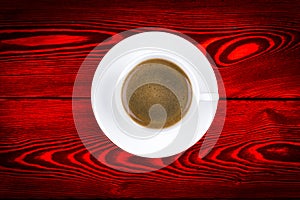 Overhead view of a freshly brewed mug of espresso coffee on red rustic wooden background with woodgrain texture. Coffee break