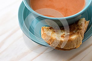 Overhead view of half a grilled cheese sandwich and tomato soup. Served on a wood table. Copy space.