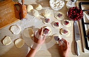 An overhead view of the hands of a pastry chef placing cherries on rolled round molds of dough as one of the stages of making