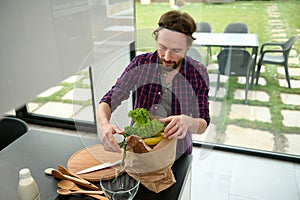 Overhead view of a handsome European guy in checkered shirt standing on the kitchen in a spacious villa and unpacking the eco pack