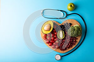Overhead view of healthy food on heart shaped cutting board by stethoscope on blue background
