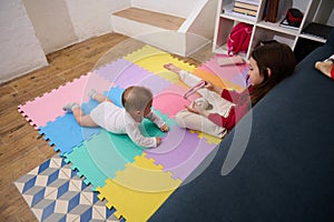 Overhead view of a little child girl, loving caring sister playing with her baby boy brother on a colorful puzzle