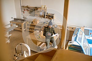 Overhead view on man carpenter sitting on table at modern joinery workshop