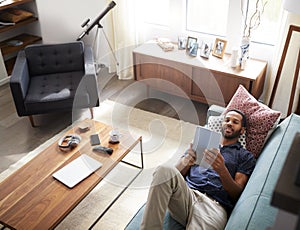 Overhead View Of Man Lying On Sofa At Home Watching Movie On Digital Tablet