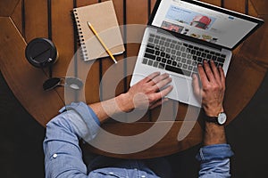 overhead view of man using laptop with ebay website while sitting at table with coffee