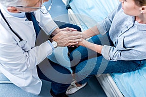 overhead view of mature male doctor holding hands of female patient in hospital