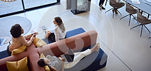 Overhead View Of Modern Open Plan Office With Female Staff Working In Breakout Seating Area