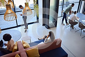 Overhead View Of Modern Open Plan Office With Staff Working Around Table And Breakout Seating Area