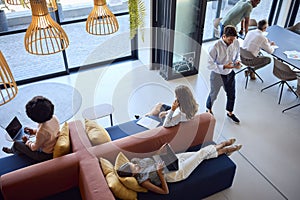 Overhead View Of Modern Open Plan Office With Staff Working Around Table And Breakout Seating Area