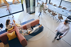 Overhead View Of Modern Open Plan Office With Staff Working Around Table And Breakout Seating Area