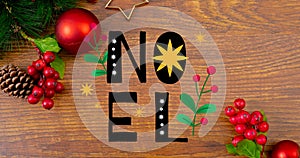 Overhead view of noel text over cherries and pine cones with baubles on wooden table