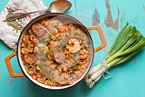 Overhead view of an orange enamel cast iron pot filled with Cajun etouffee, scallions and spoon on a turquoise table.