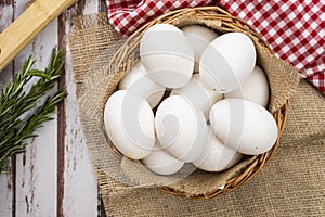 Overhead view of organic farm white eggs in a basket on a rustic wooden table with rosemary