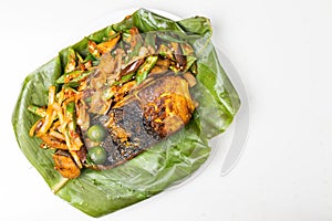 Overhead view of popular grilled stingray fish with spices and vegetable served on banana leaf