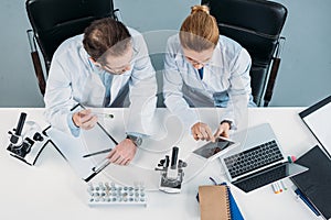 overhead view of scientific researchers in white coats using tablet together at workplace