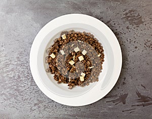 Overhead view of a serving of sweet chocolate granola with pieces of white chocolate in a bowl on a gray tabletop