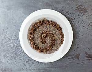 Overhead view of a serving of sweet chocolate granola in a white bowl on a gray tabletop