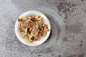 Overhead view of a small white bowl filled with walnuts on a gray mottled tabletop