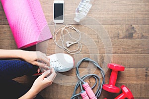 Overhead view of sport and fitness woman tying shoes with mobile devices and sport equipments on wooden