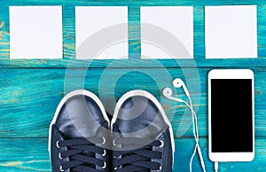 Overhead view of sports shoes by mobile phone with isolated screen and in-ear headphones and white empty blank sheets