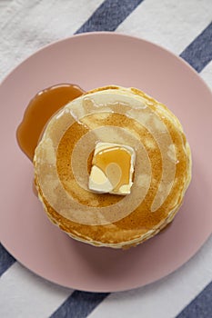Overhead view, stack of homemade pancakes with butter and maple syrup on a pink plate. Overhead, top view, flat lay. Closeup