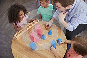 Overhead View Of Teacher And Pupils At Desk In Montessori School