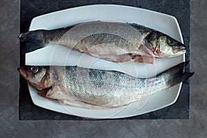 Overhead view of two pieces of sea bass on a white ceramic platter with a vintage black and gray marble texture background.