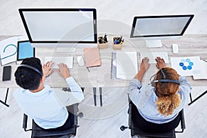 Overhead view of two unknown business people working on computers on a desk in a office. Two colleagues wearing headsets