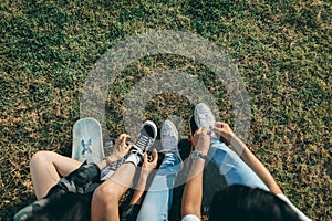 Overhead view of two young skateboarders tying shoelaces while sitting on the grass in a park