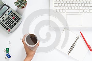 Overhead view of woman hand holding cup of coffee with laptop