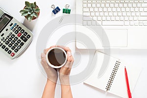 Overhead view of woman hand holding cup of coffee with laptop