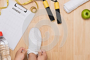 Overhead view of woman hands tying shoes with sport equipments o