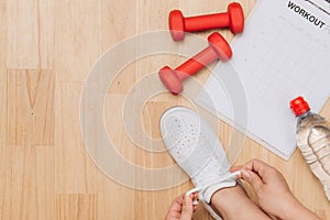 Overhead view of woman hands tying shoes with sport equipments o