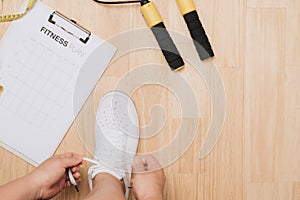 Overhead view of woman hands tying shoes with sport equipments on wood background