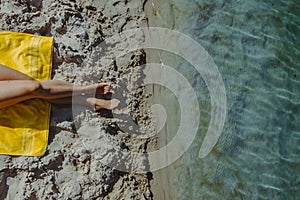 overhead view woman legs at yellow blanket at sand beach blue sea water
