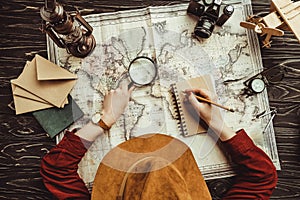 overhead view of woman making notes in notebook with blank envelopes, map and photo camera