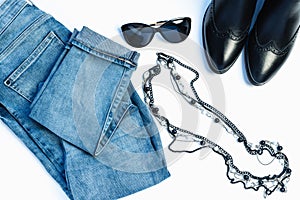 Overhead view of woman`s casual outfit on white background - glasses, blue jeans, necklace and leather chelsea boots