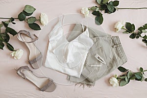 Overhead view of woman's casual spring summer outfit. Jeans, sandals, accessories and flowers on beige background. Flat