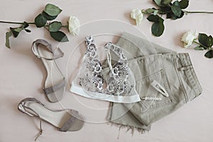 Overhead view of woman's casual spring summer outfit. Jeans, sandals, accessories and flowers on beige background. Flat