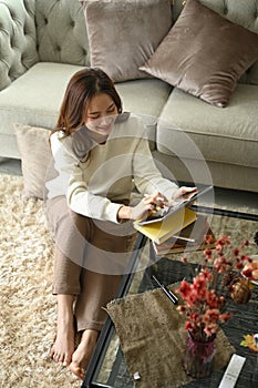 Overhead view of young woman sitting on floor in living room and using digital tablet leisure time in autumn day