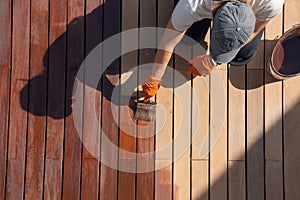 Overhead worker applying protective deck stain color on wood planks