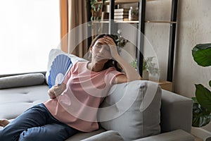 Overheated Arabian woman waving paper fan, sitting on couch