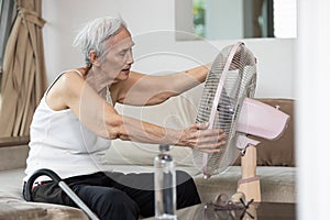 Overheated asian senior woman sweating,high temperature in sunny day while stay at home,cooling herself in front of an electric