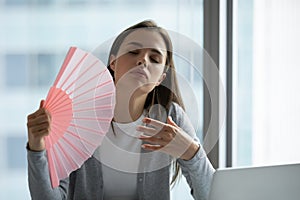 Overheated female employee breathe fresh air from hand fan