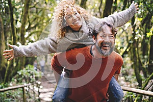 Overjoyed adult couple have fun together at outdoor park in leisure activity. Man carrying woman in piggyback and laugh a lot.