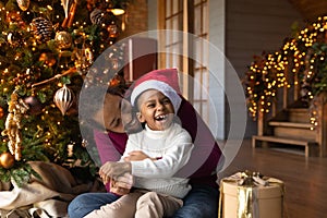 Overjoyed African American man hugging son, celebrating Christmas, opening gifts
