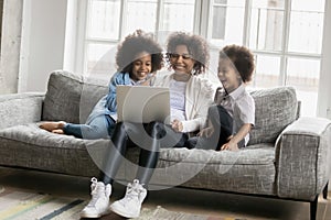 Overjoyed African American woman with two little kids using laptop