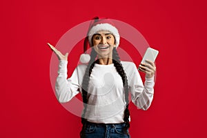 Overjoyed Arab Woman In Santa Hat Holding Smartphone And Exclaiming With Excitement